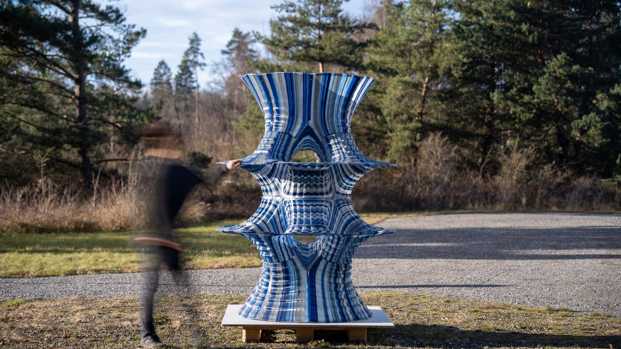 A two-metre printed shell with flaring, saddle-shaped tiers and blue and silver print lines, standing outdoors as a person walks past