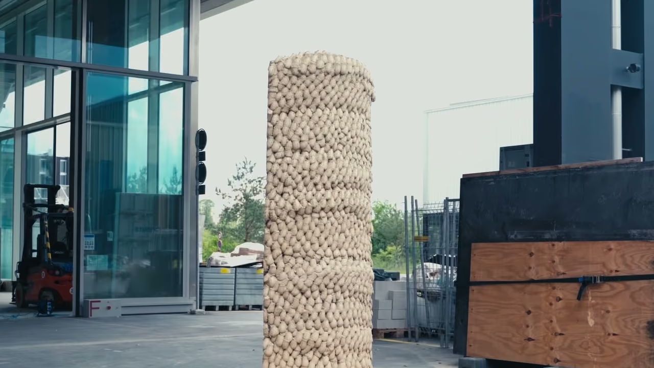 A column built from thousands of compressed earth portions standing on a pallet outside a laboratory hall