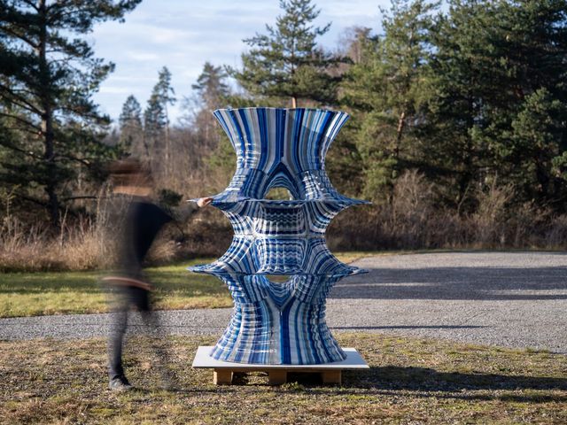 A two-metre printed shell with flaring, saddle-shaped tiers and blue and silver print lines, standing outdoors as a person walks past